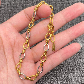 Gold and silver two-tone link bracelet with twisted connectors, held in hand against textured gray background